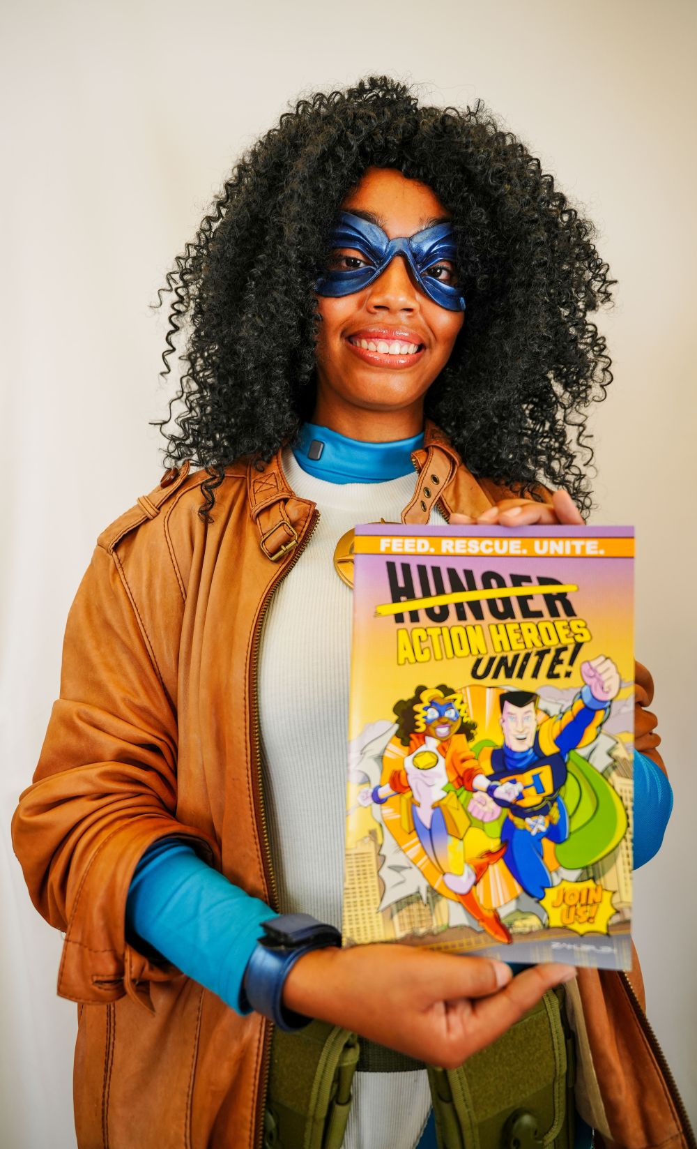 Person wearing a superhero costume holding a comic book with a superhero theme.
